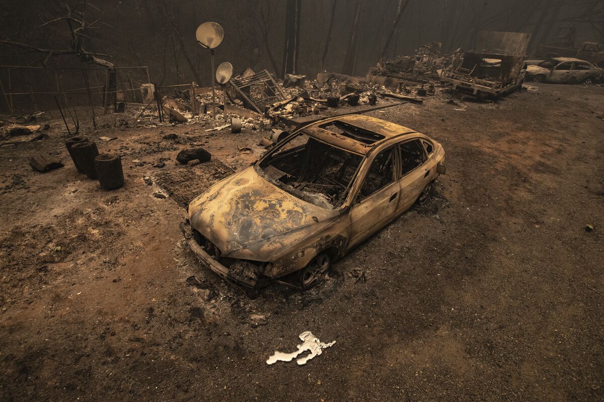 A scorched car sits in front of the remnants of a burned home 