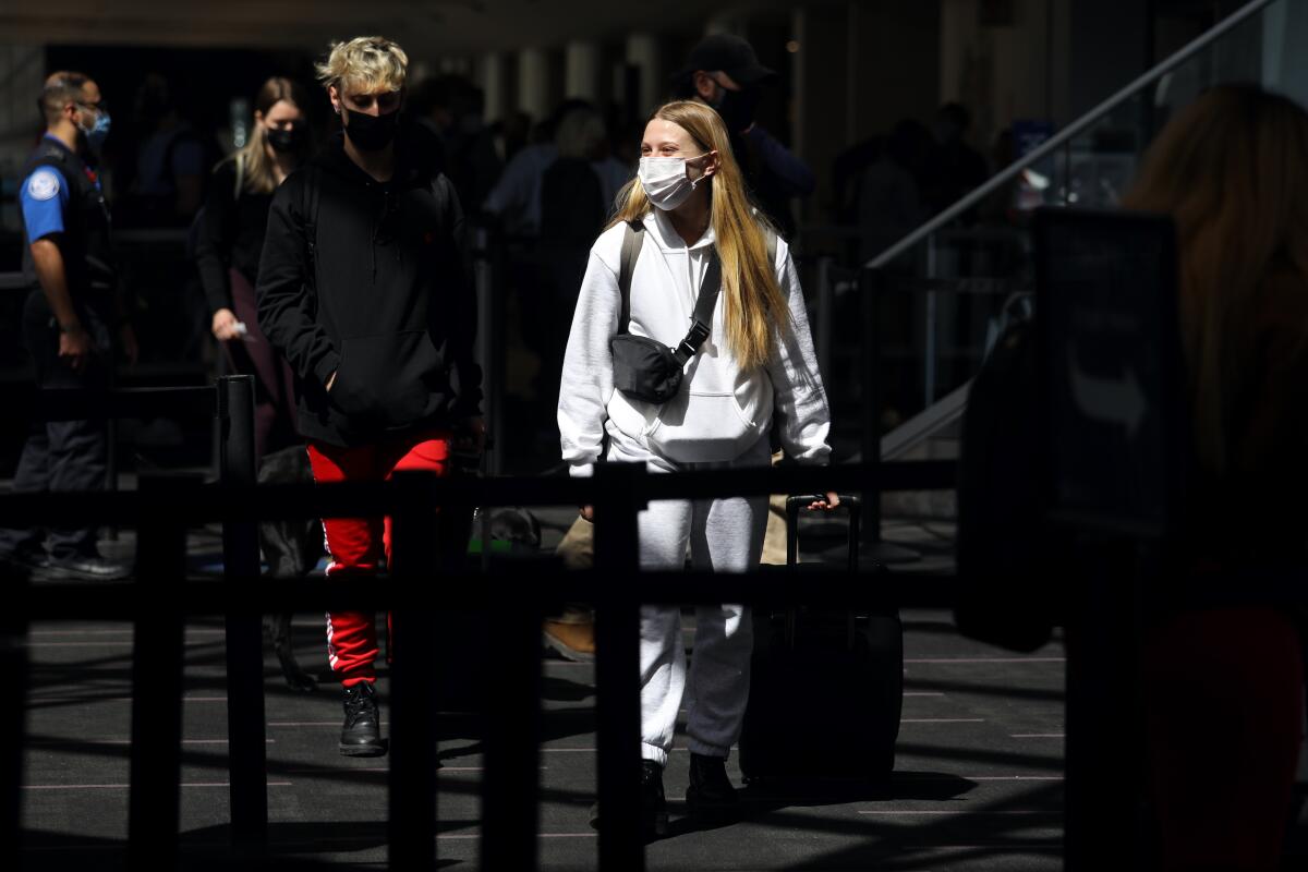 A young man in a black sweatshirt and red sweatpants and a woman wearing a white sweat suit wear facemasks.
