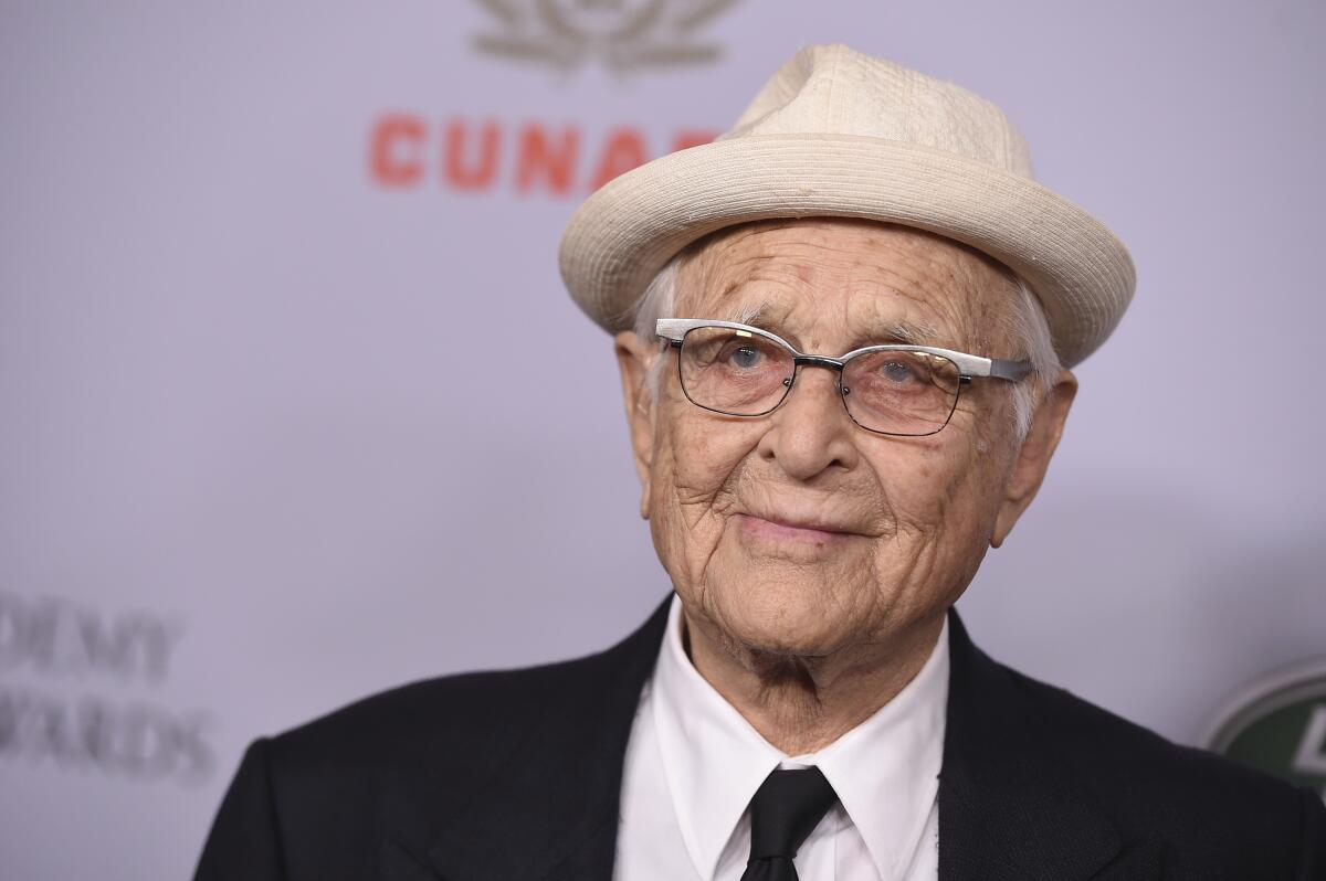 Norman Lear in a white hat and glasses in front of a purple backdrop.