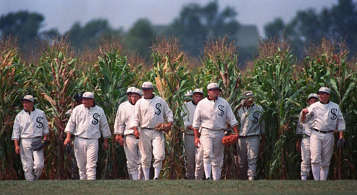 Men in baseball uniforms emerge from a cornfield
