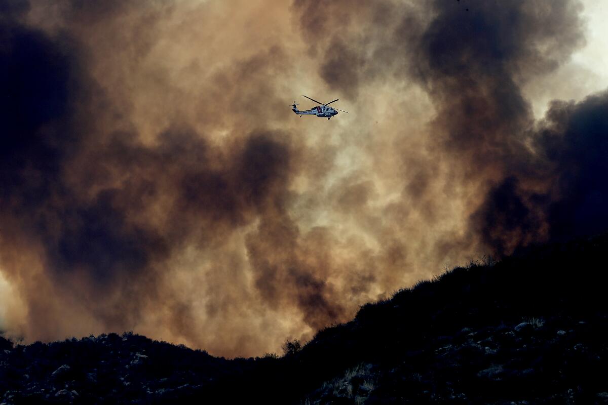  A firefighting helicopter is dwarfed by the plume of the Fairview fire.