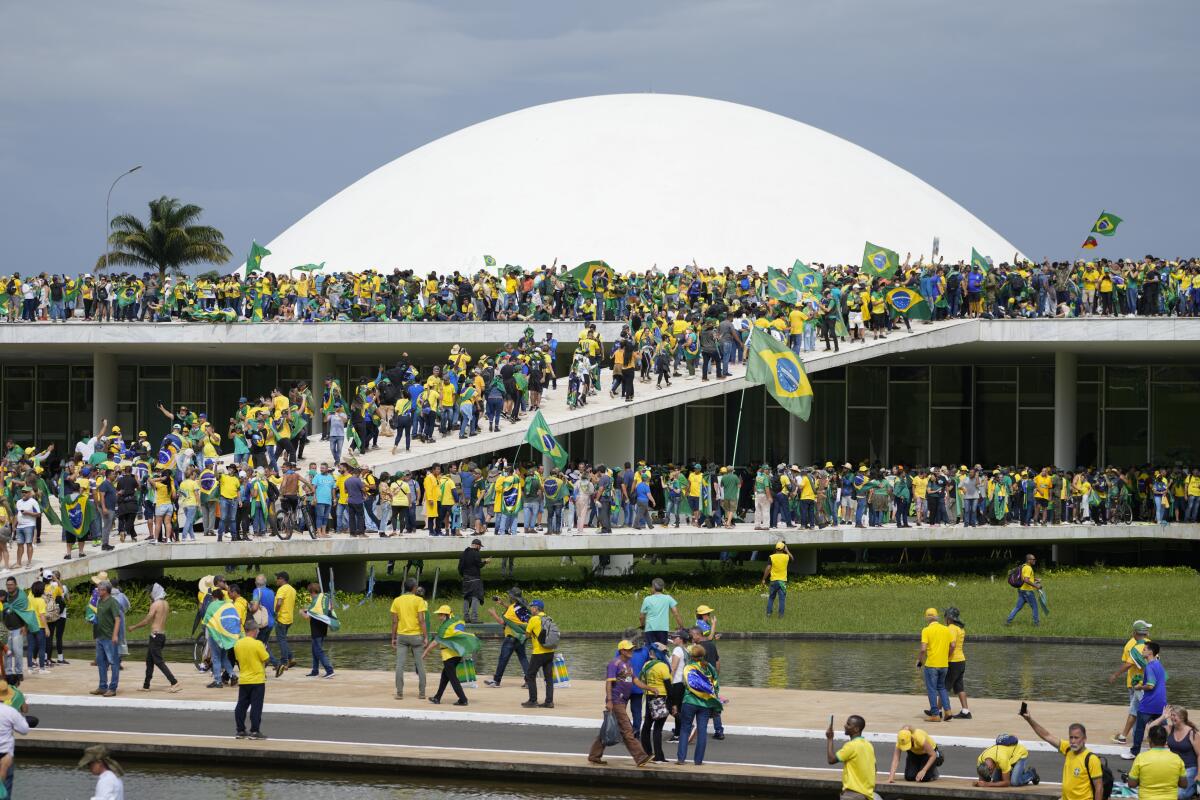 People wearing yellow and green crowd the roof and walkways of the National Congress building in Brasilia, Brazil.
