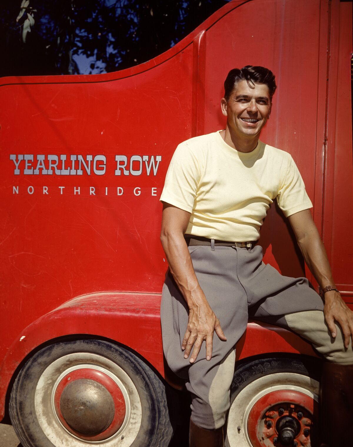 Ronald Reagan, wearing jodhpurs and riding boots, poses in front of a red trailer at the Yearling Row Ranch in Northridge, circa 1960.
