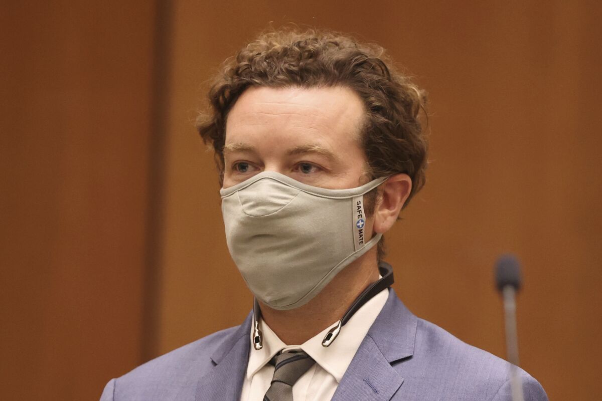 Danny Masterson seen from the shoulders up, wearing a mask and a tie and jacket