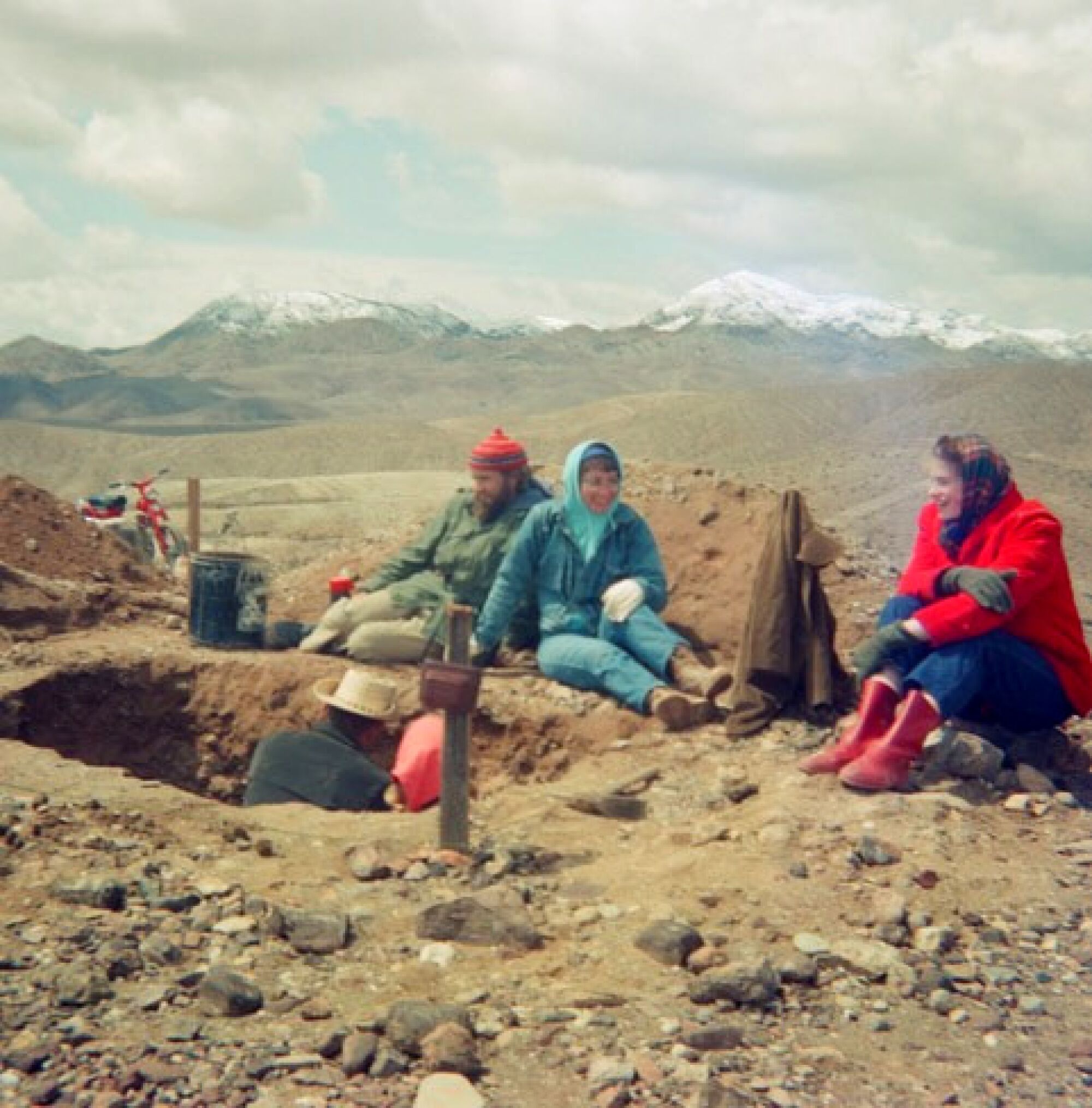 A man inside an excavation pit, with three people sitting on the dirt nearby.