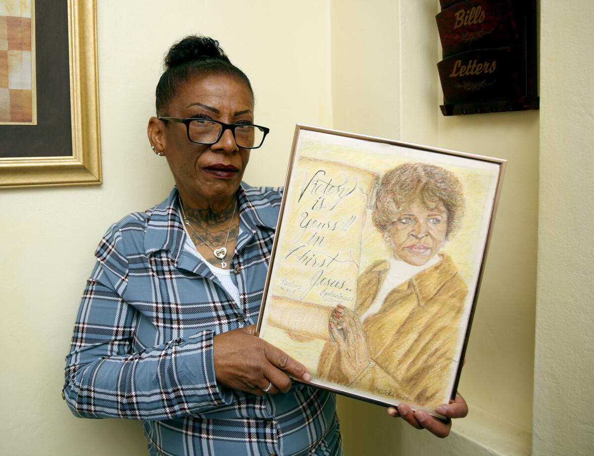 A woman holds up a portrait of another woman.