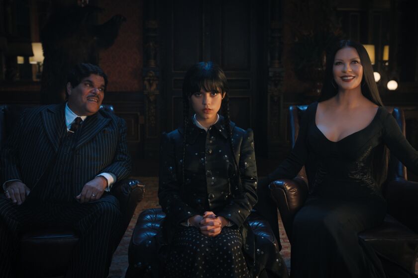 A creepy father and mother sit in leather chairs while their creepy daughter sits on an ottoman between them and stares