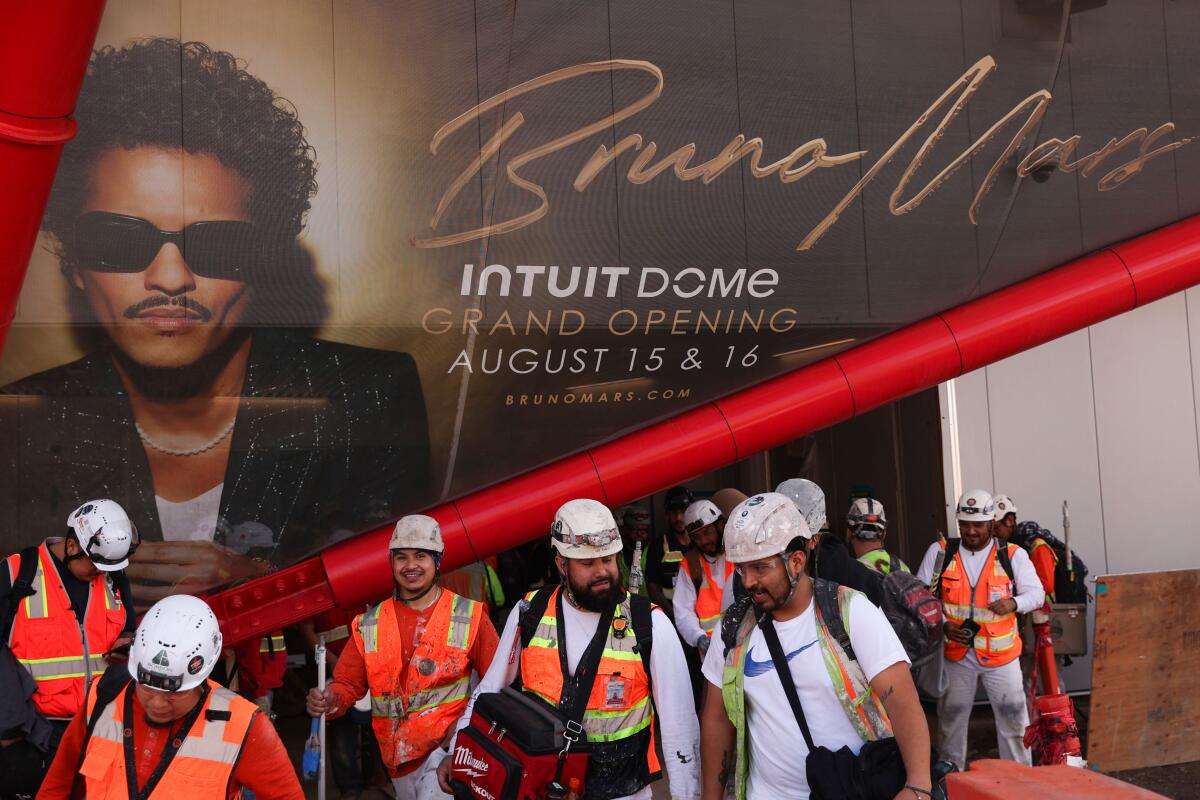 Construction workers walk by an advertisement for Bruno Mars' Thursday-night performance at Inglewood's Intuit Dome.