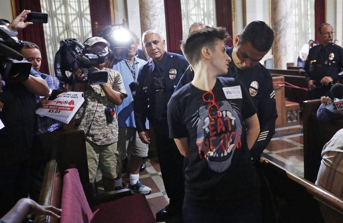 Police put handcuffs on a protester as TV cameras record the scene.