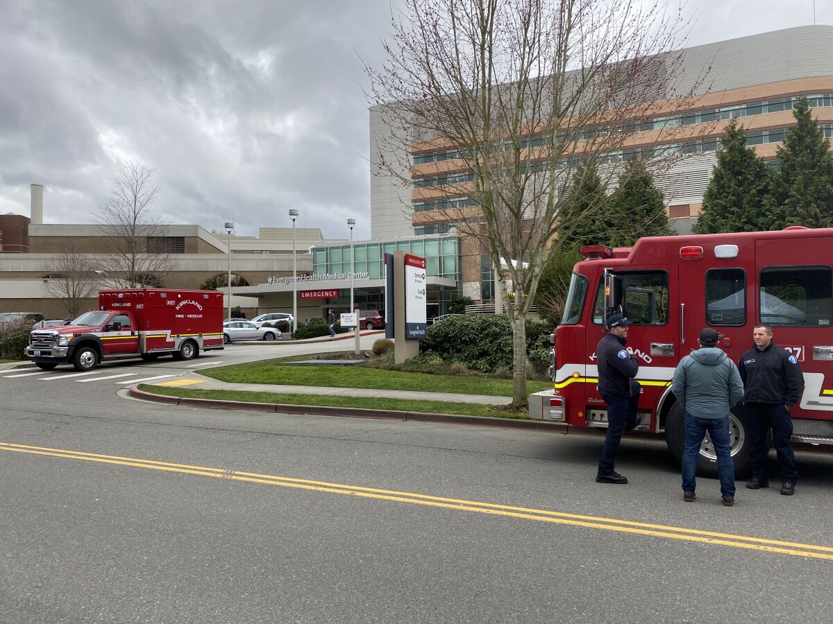 Kirkland, Wash., firefighters talk with a passerby Tuesday after transporting a patient to EvergreenHealth, where residents of a local nursing home have died after contracting COVID-19. A quarter of the Seattle suburb's firefighters are in quarantine at home after being exposed to coronavirus, and some have flu-like symptoms.