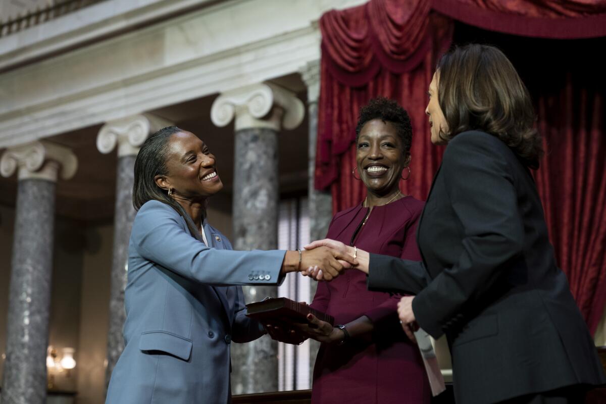 Laphonza Butler shakes hands with Vice President Kamala Harris in an ornate room as Butler's wife, Neneki Lee, stands by