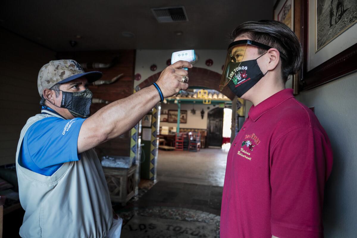 Nicolas Montaño uses a forehead scanner to check Diego Almendor's temperature 