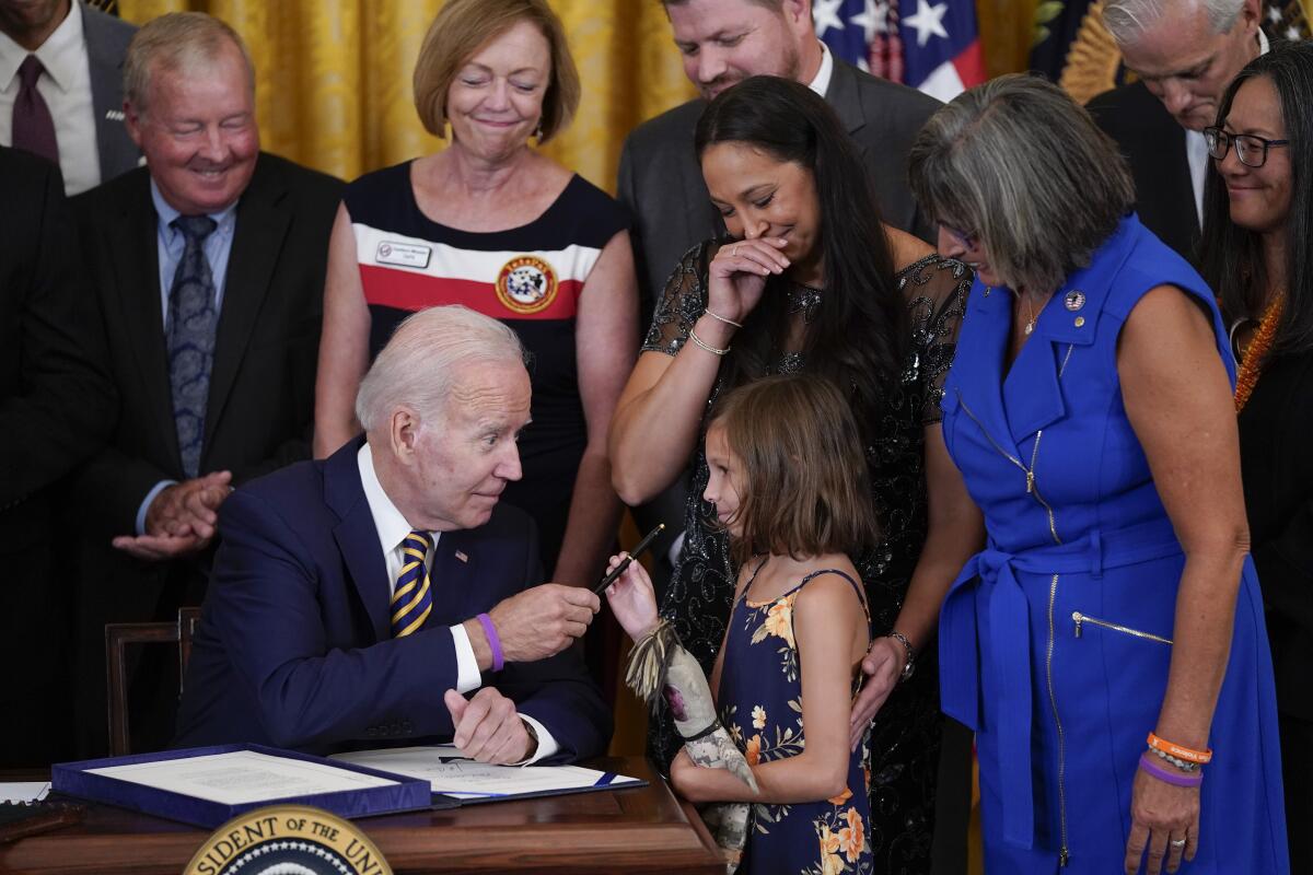 President Joe Biden gives the pen he used to sign the "PACT Act of 2022" to Brielle Robinson, daughter of Sgt. 1st Class Heath Robinson, who died of cancer two years ago, during a ceremony in the East Room of the White House, Wednesday, Aug. 10, 2022, in Washington. (AP Photo/Evan Vucci)