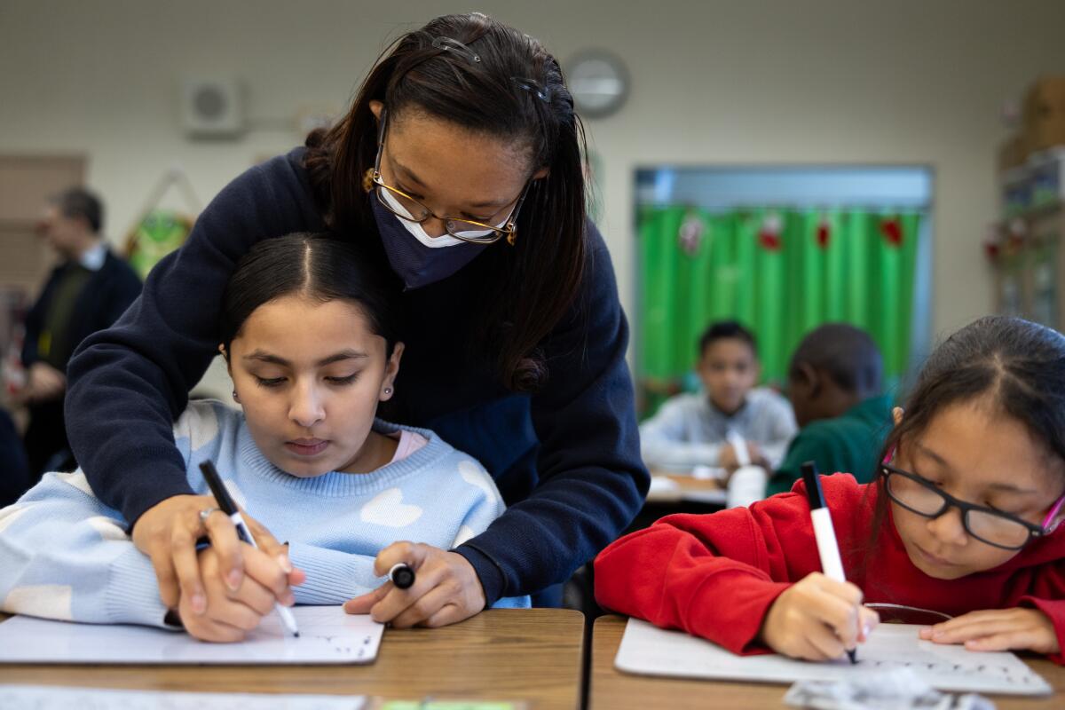 Tyara Brooks helps guide fourth-grade student Aaliyah Miranda-Garcia, left, and Sophia Ortega during a lesson on cursive writing.