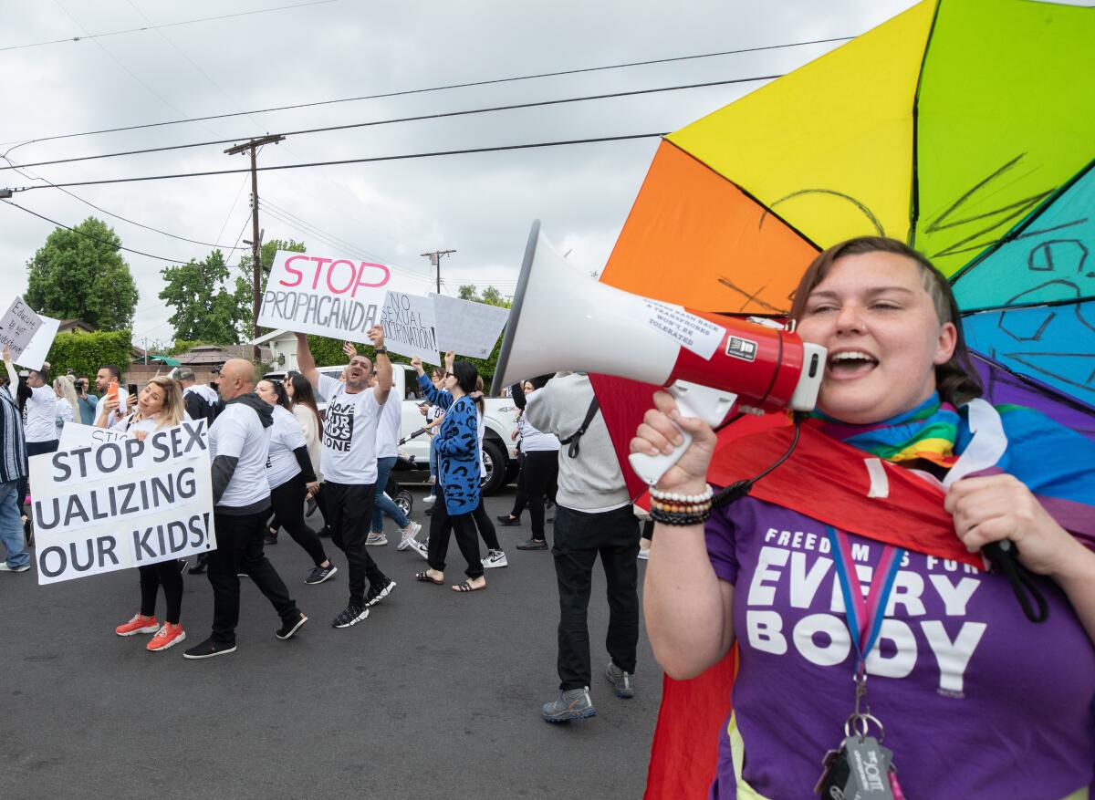 Protesters with signs such as "Stop sexualizing our kids" and counter-protesters, one with a rainbow umbrella