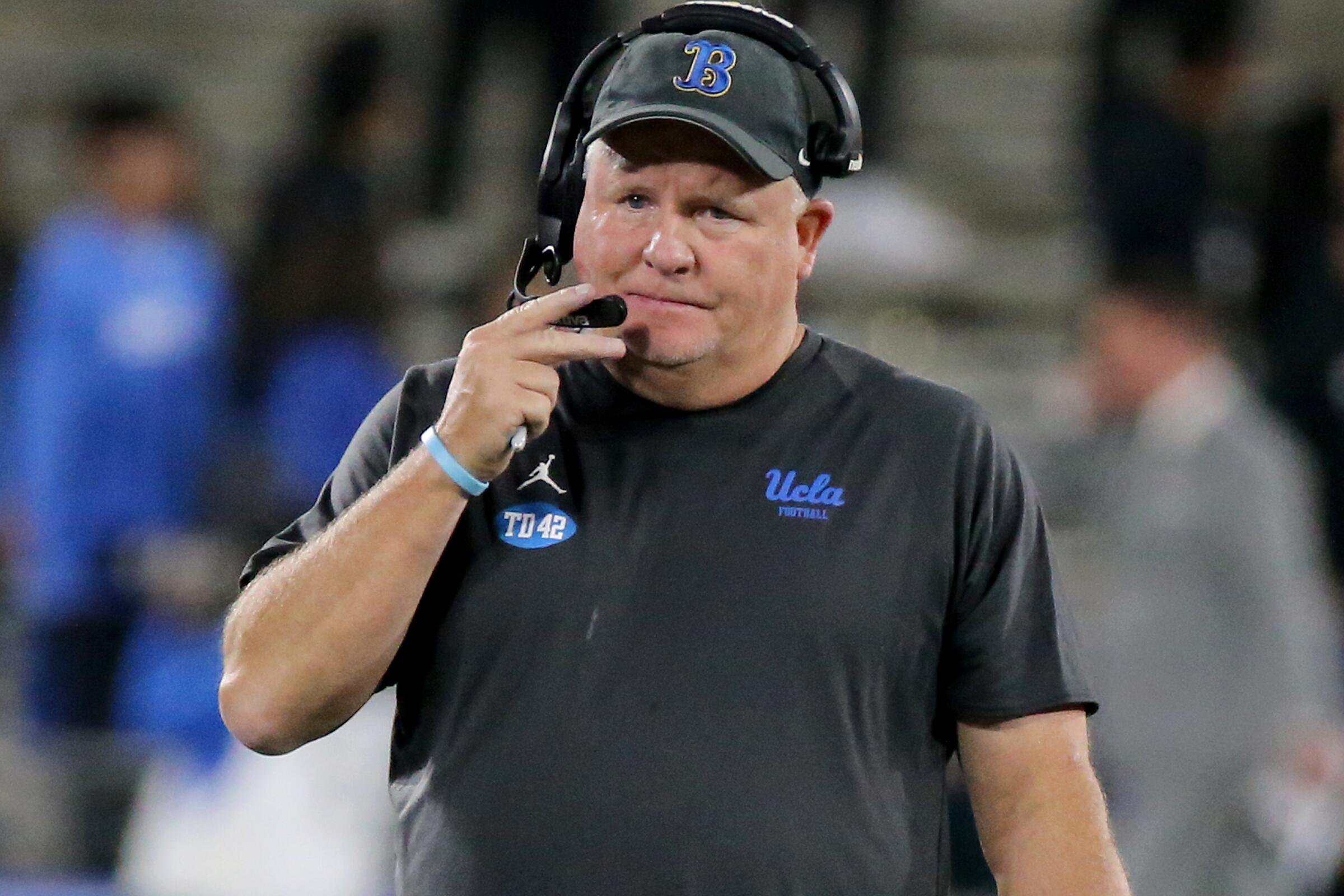 UCLA head coach Chip Kelly talks on his headset while walking the sideline.