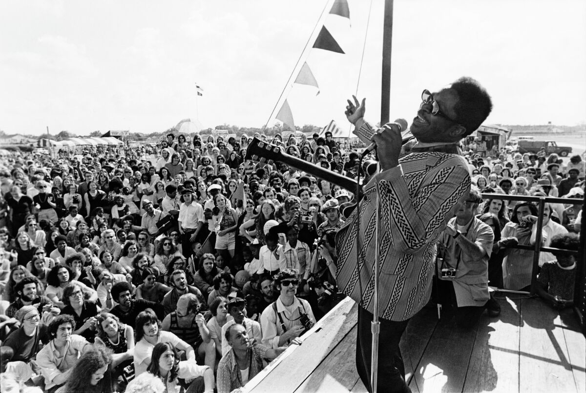 A man with a guitar performs before a large outdoor audience in the documentary “Jazz Fest: A New Orleans Story.”