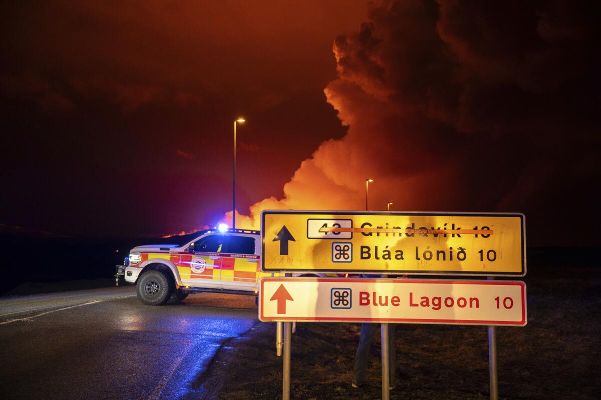 An emergency vehicle blocks a road with orange smoke visible in the distance.