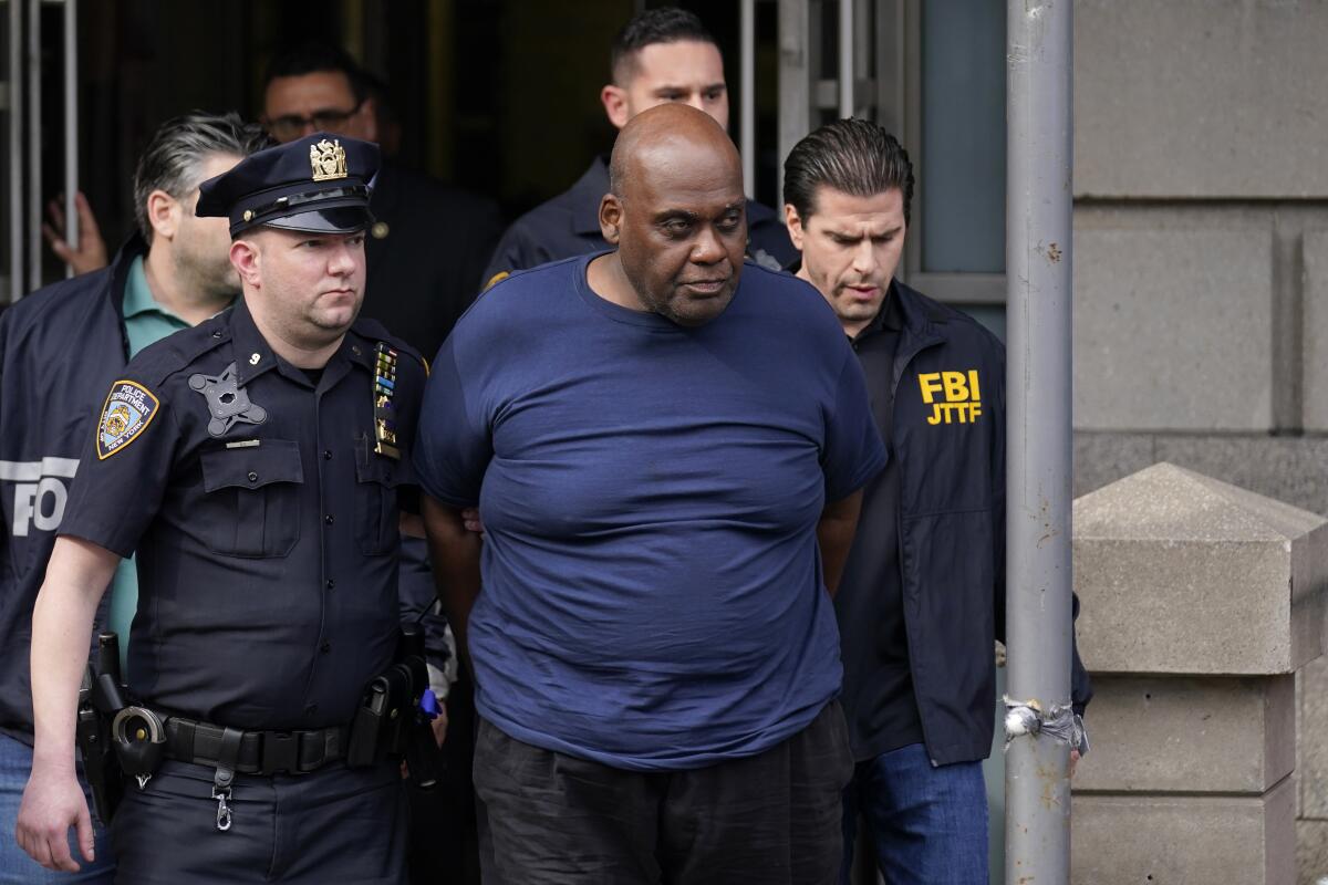 Law enforcement officials lead a man in a T-shirt away from a police station in New York.