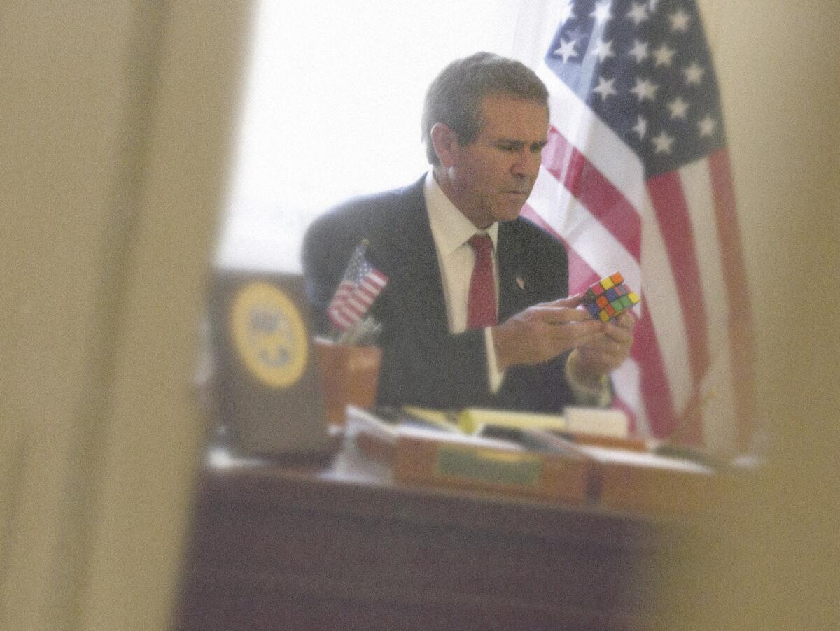 The photograph "Bush Rubik" shows a George W. Bush look-alike playing with a Rubik's Cube.  