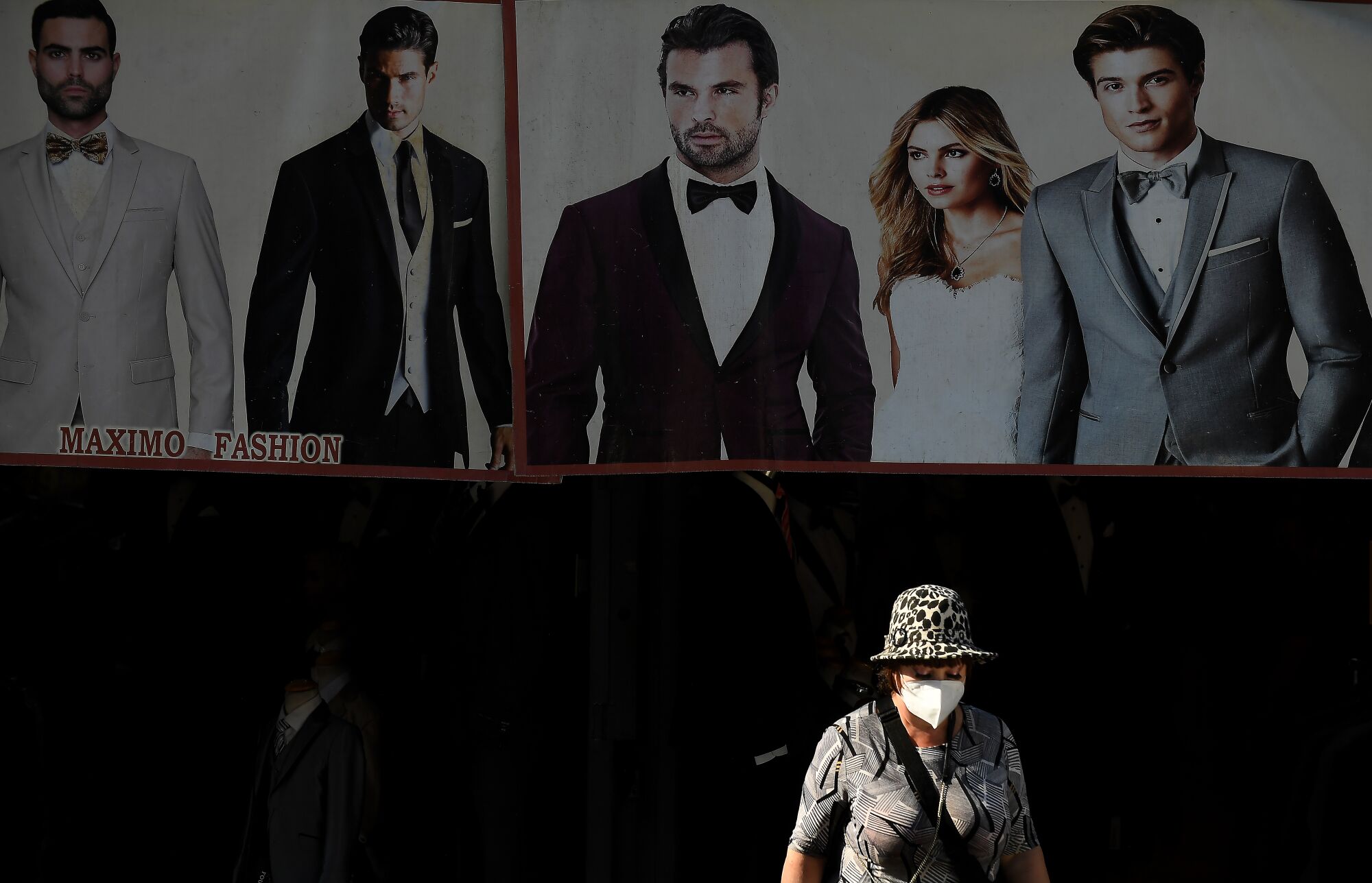 An advertisement of people in formal wear provides a backdrop for a masked pedestrian.