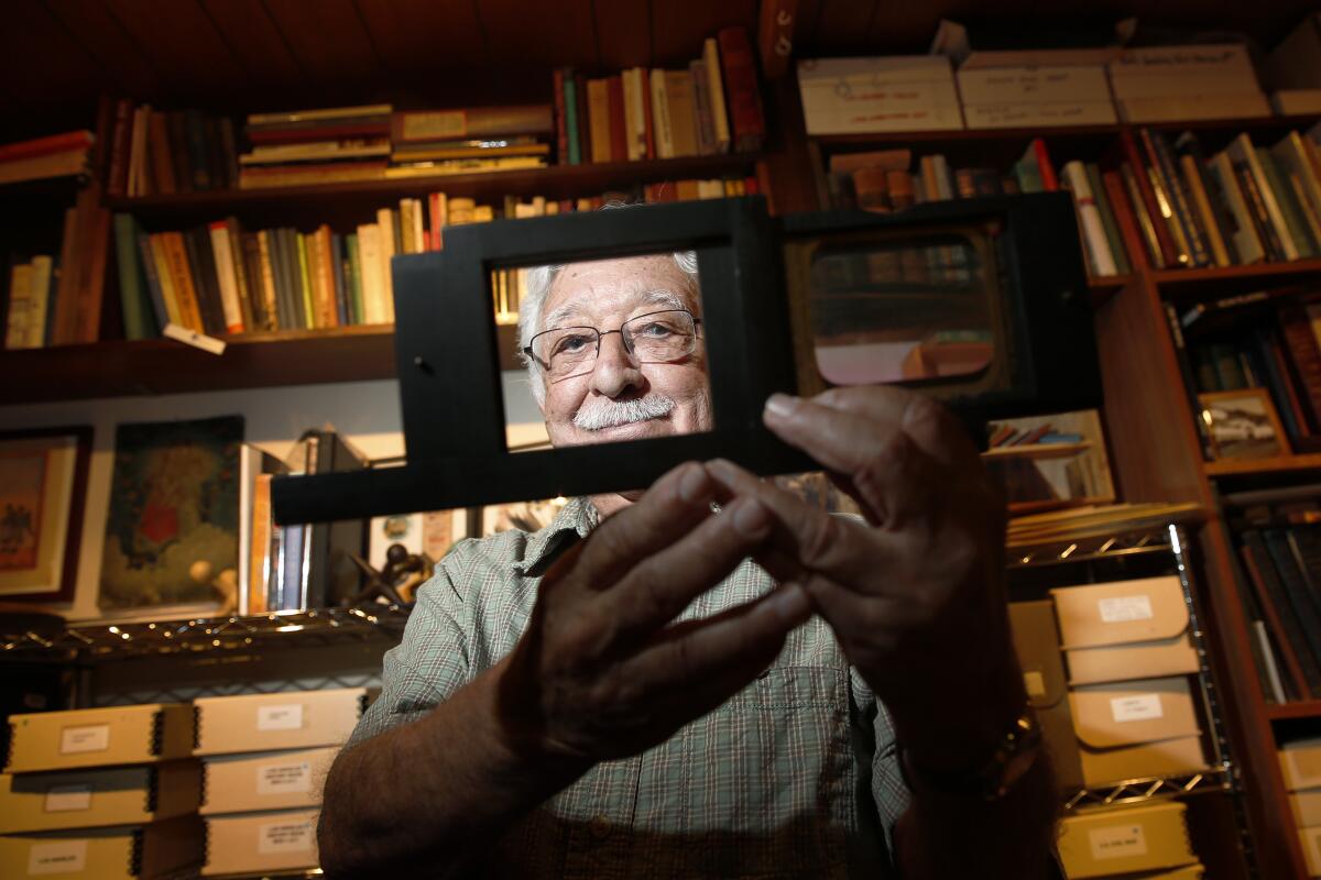 A man holds a frame in front of his face, with bookcases behind him.