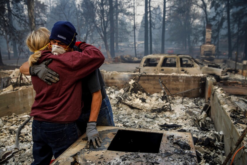 Michael John Ramirez hugs his wife, Charlie, as they search the rubble of their destroyed home in Paradise, Calif.