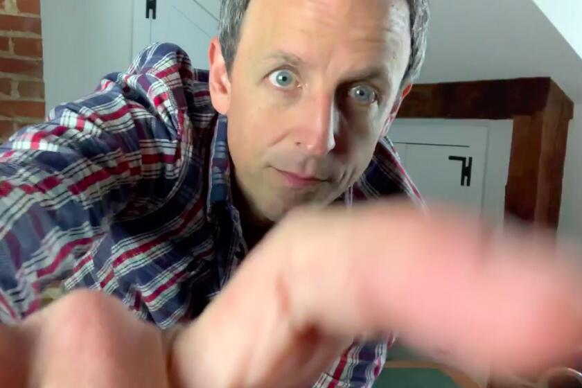 Seth Meyers fiddles with his iPad mounted on a tripod shooting “Late Night with Seth Meyers” produced from his attic.