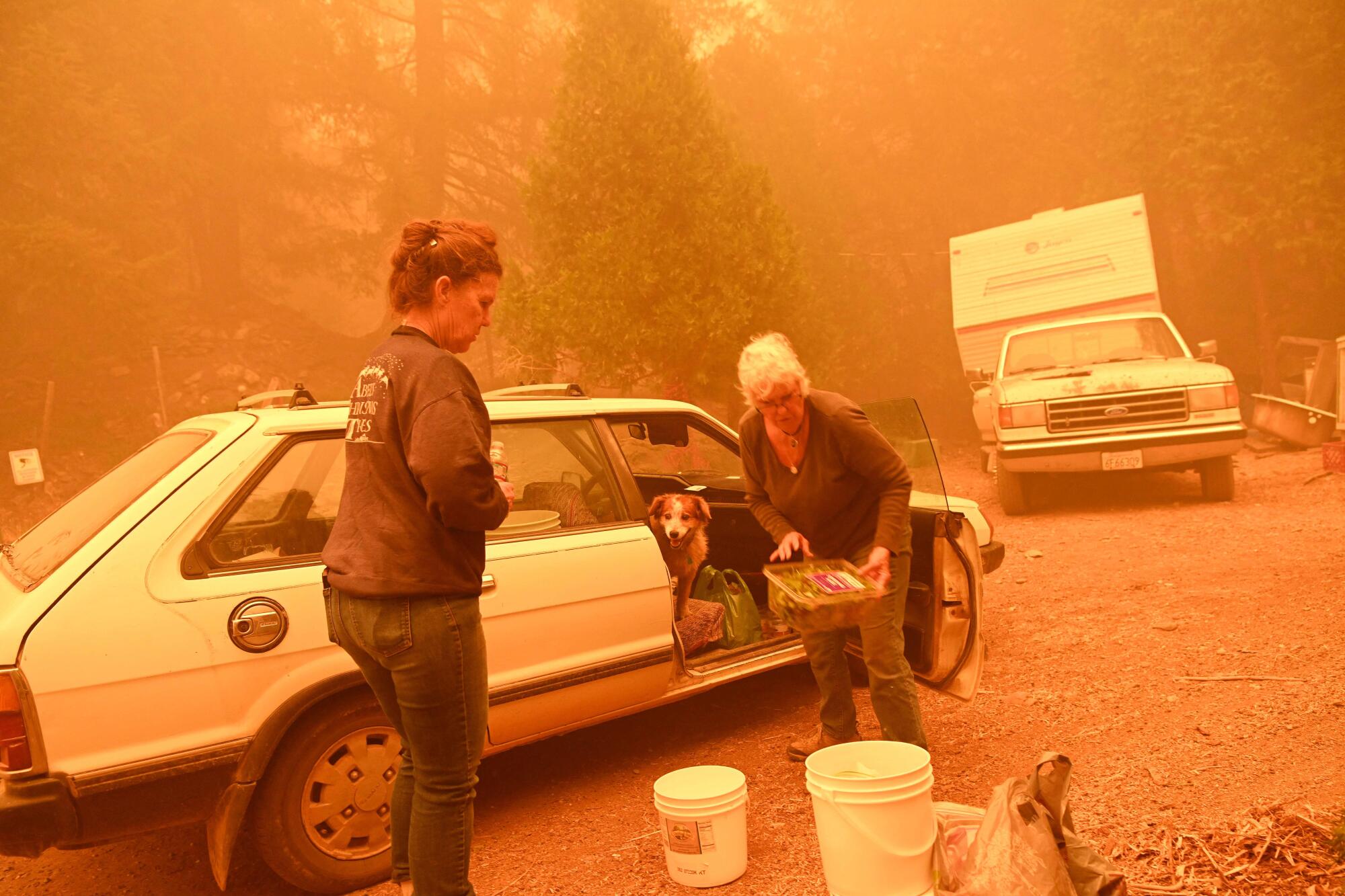 Resident Pamela Aylen, right, delivers supplies to one of her neighbors as the two prepare to ride out the Dixie fire