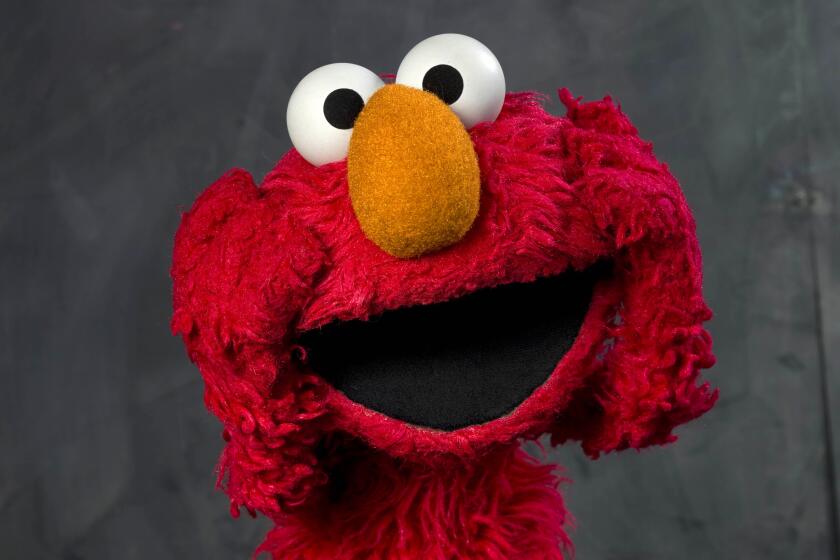 The red muppet named Elmo holds his furry hands to his face while opening his mouth