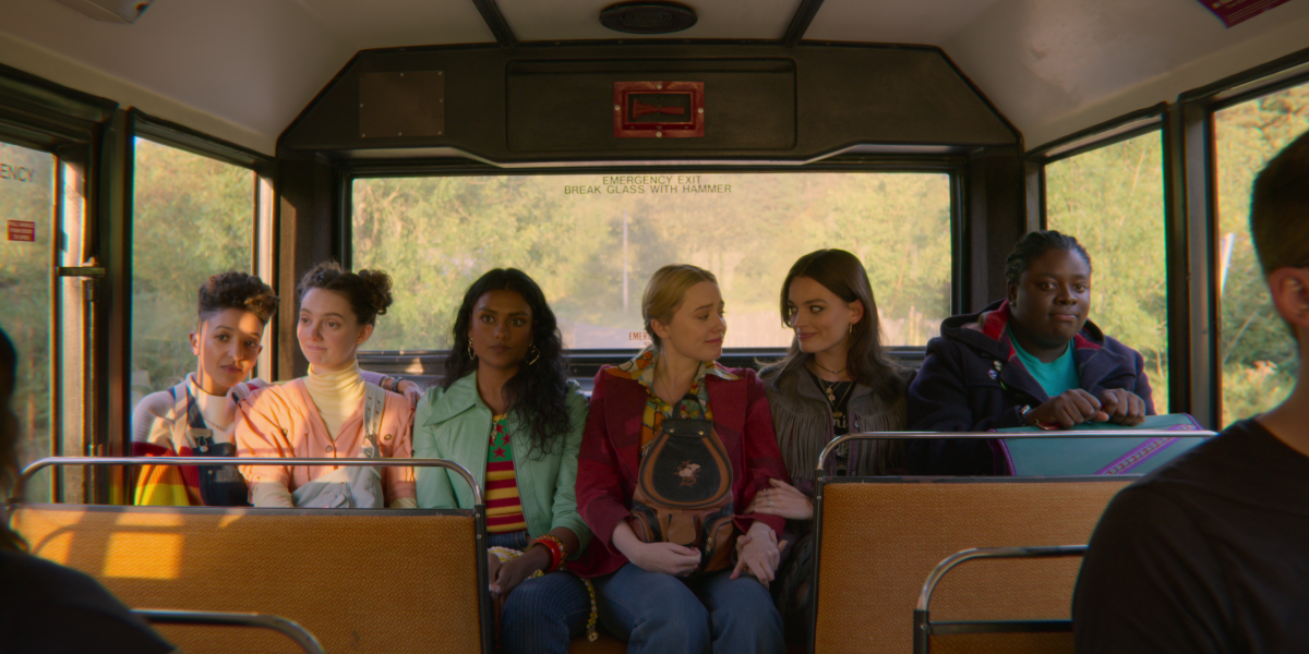 Six girls sitting in a row in the back of a public bus.