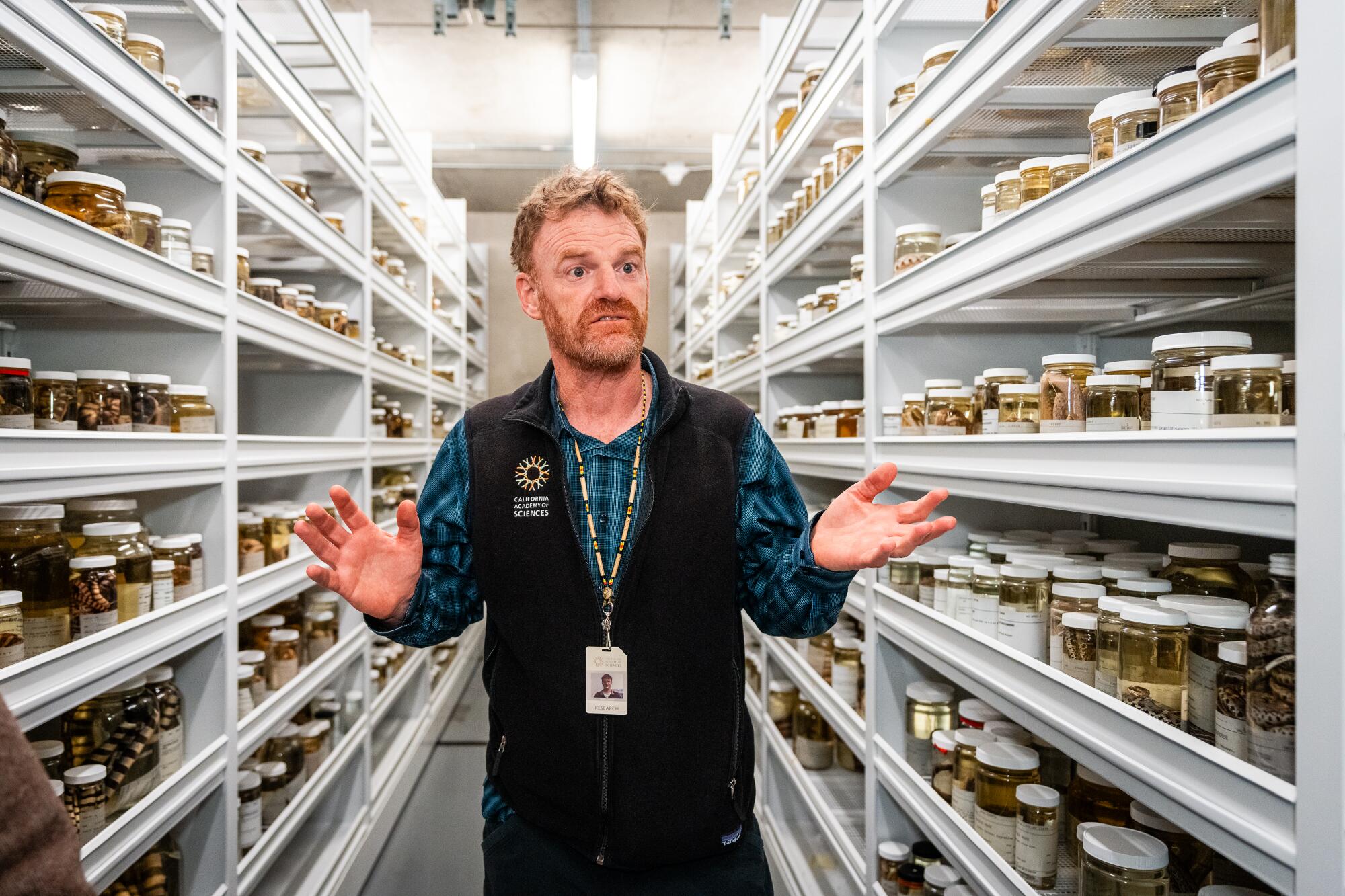 A man stands amid shelves of snake specimens.