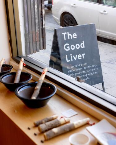 Merchandise on display in the front window of the Good Liver, with a sandwich board visible outside.