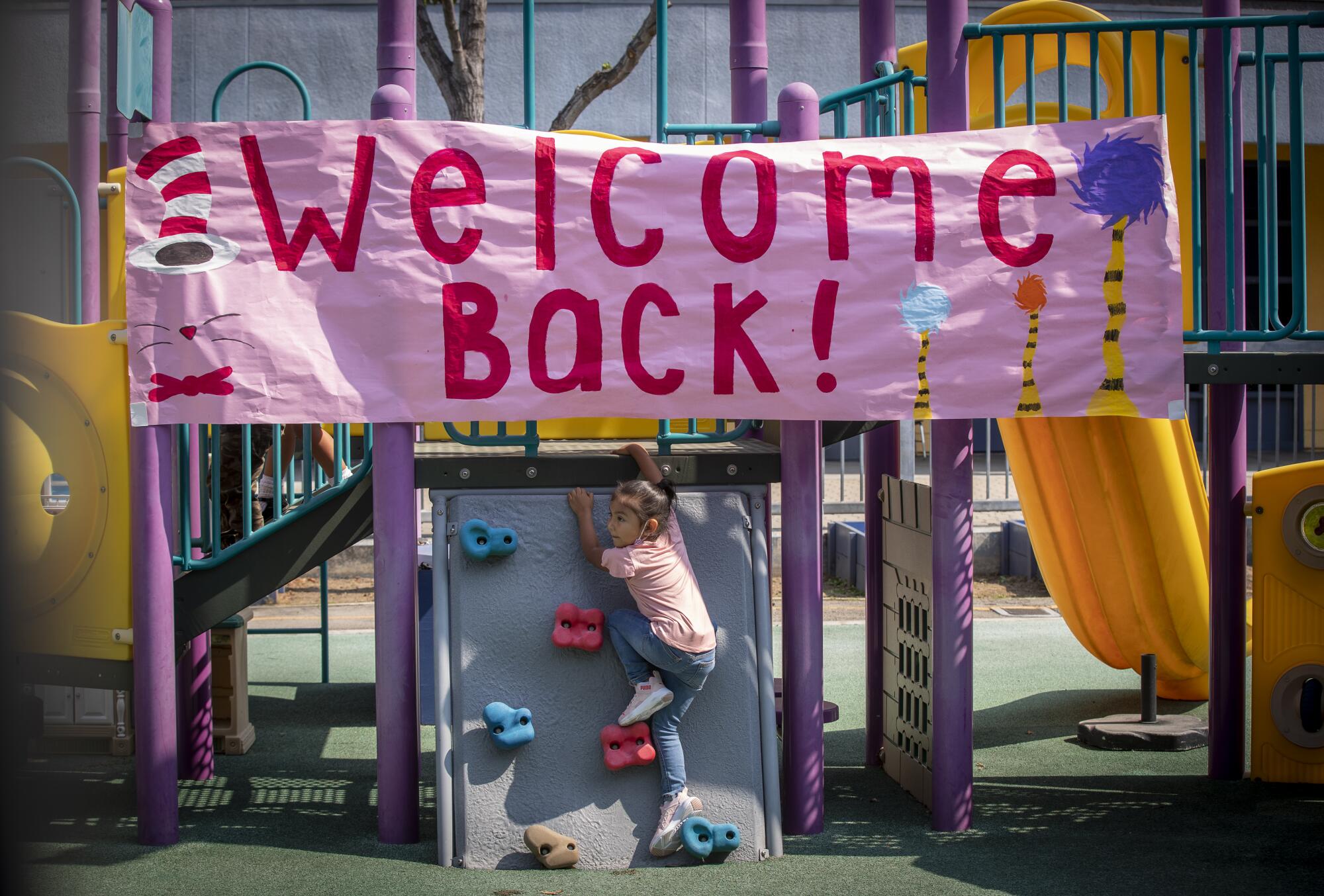 A child climbs on playground equipment underneath a giant Welcome Back banner
