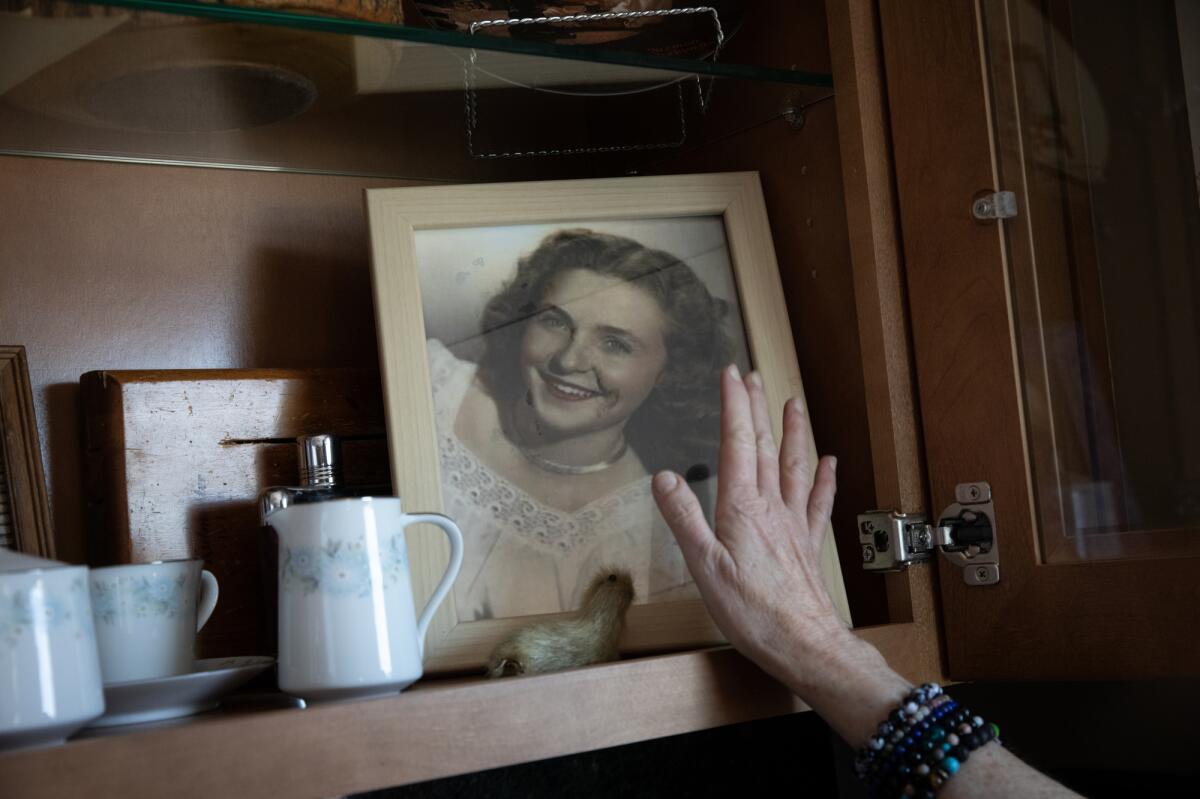 Mementos of a woman's parents are arranged on a shelf, as her hand rests her her late mother's photo.