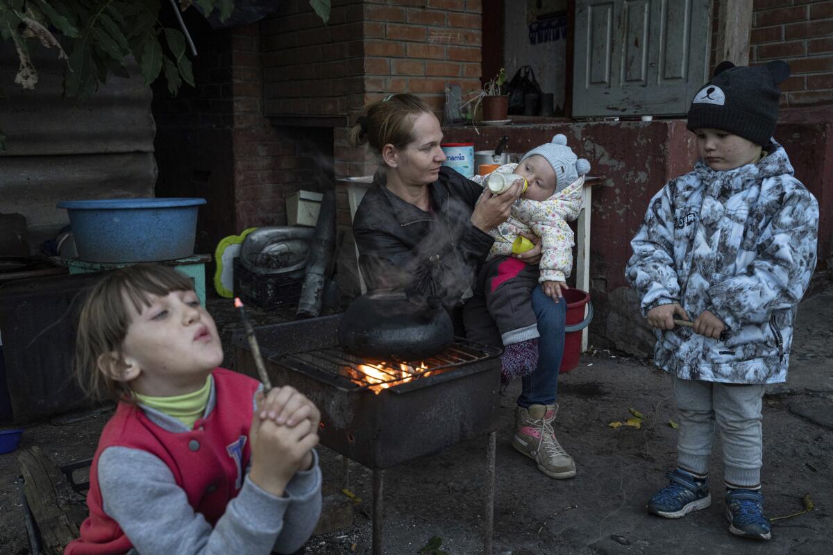 A woman feeds her 9-month-old daughter as her two other children are nearby.