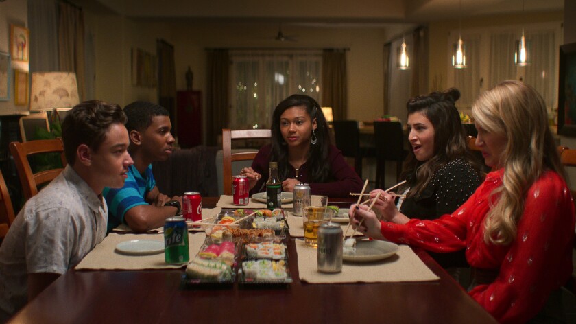 A group of teenagers sits around a dining table eating sushi.