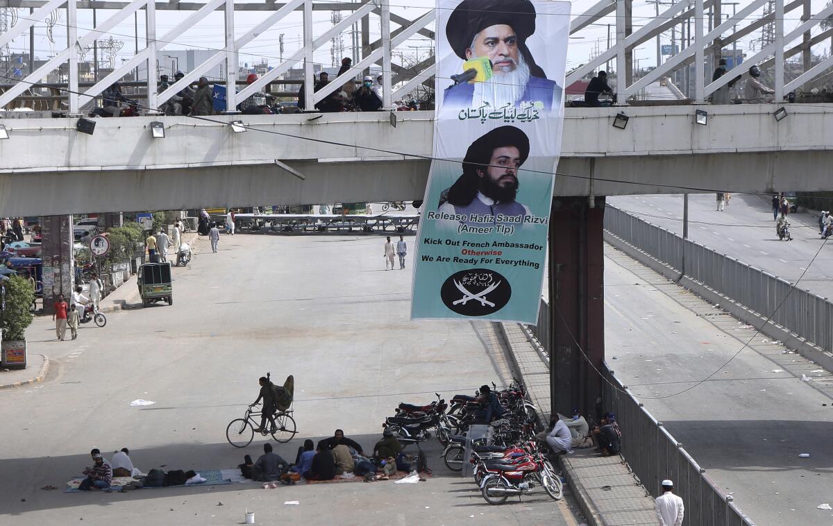 A banner with the portraits of Khadim Hussein Rizvi, top, and Saad Rizvi, leaders of Tehreek-e-Labiak Pakistan, a radical Islamist political party, hang on a bridge while their supporters block a road during a sit-in protest against the arrest of Rizvi, the head of their party, in Lahore, Pakistan, Wednesday, April 14, 2021. Pakistani security forces swinging batons and firing teargas moved before dawn Wednesday to clear sit-ins by protesting Islamists in the garrison city of Rawalpindi and elsewhere after five people died in earlier clashes, officials said. (AP Photo/K.M. Chaudary)