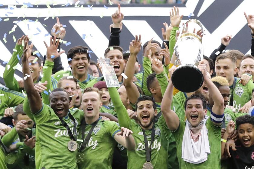 FILE - In this Nov. 10, 2019, file photo, Seattle Sounders captain Nicolas Lodeiro, right, lifts the MLS Cup trophy as he celebrates with teammates after the Sounders defeated Toronto FC in the MLS Cup championship soccer match in Seattle. Major League Soccer and its players have reached a new five-year collective bargaining agreement in time for the start of the season. The new contract must be approved by the MLS Board of Governors and the membership of the Major League Soccer Players Association. (AP Photo/Ted S. Warren, File)