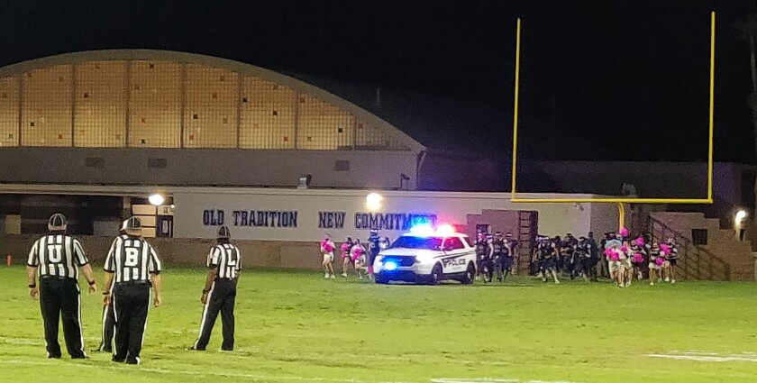 The Yuma High Criminals enter the field behind a police car.
