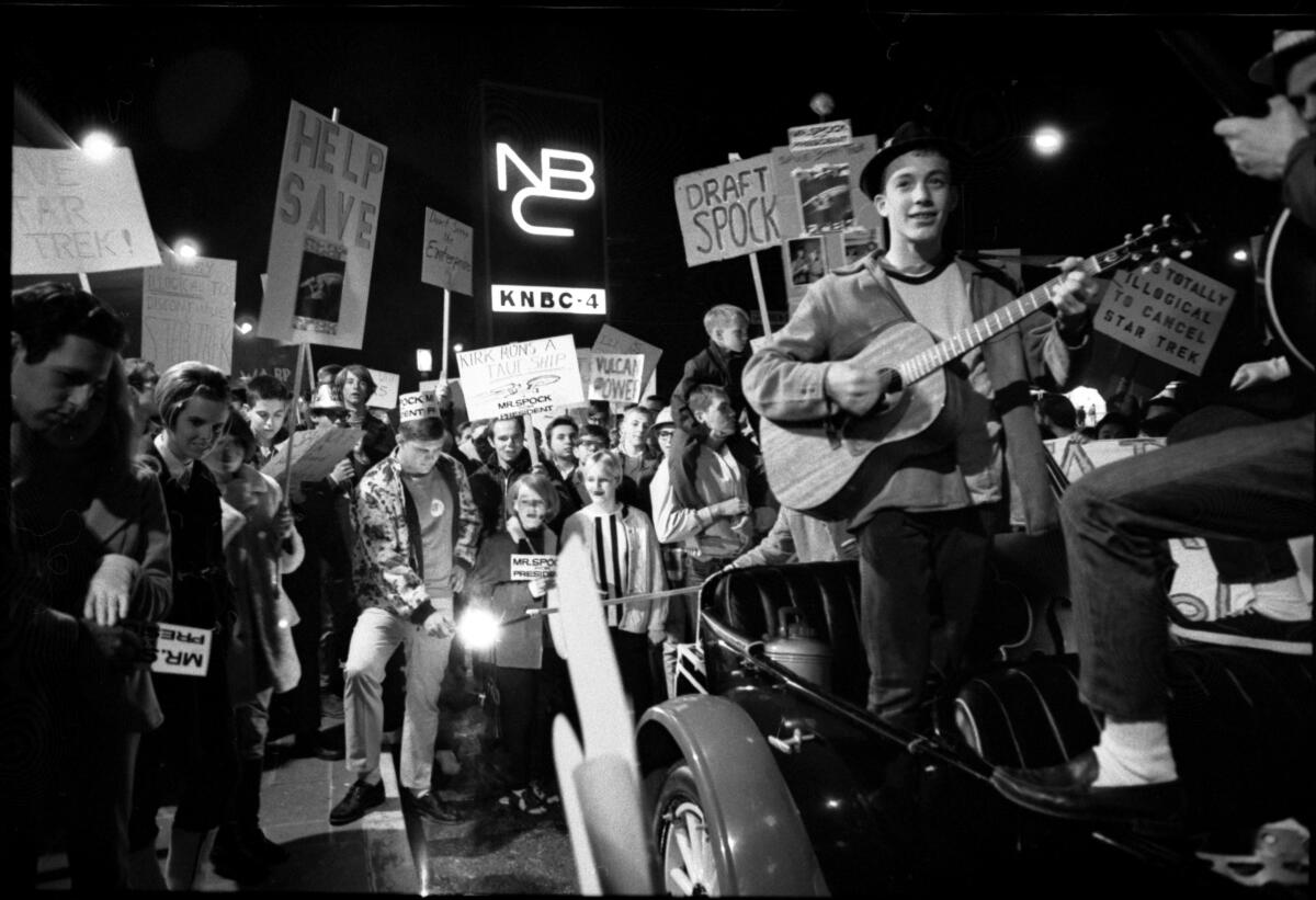 Young people carry "Star Trek"-themed signs. One young man plays a guitar. 