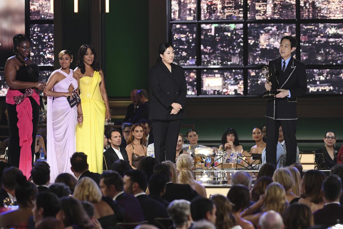  A man stands onstage to accept an award while a group of people stands to his right