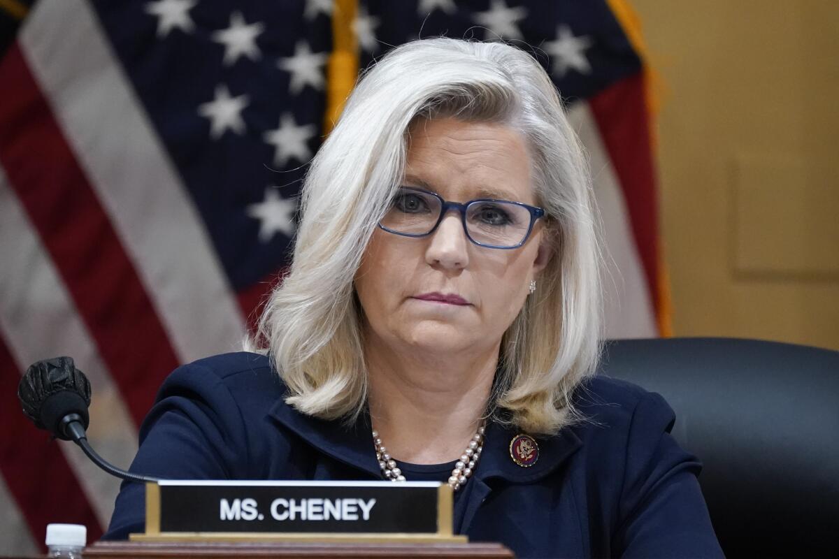 Liz Cheney sits at a dais behind her nameplate.