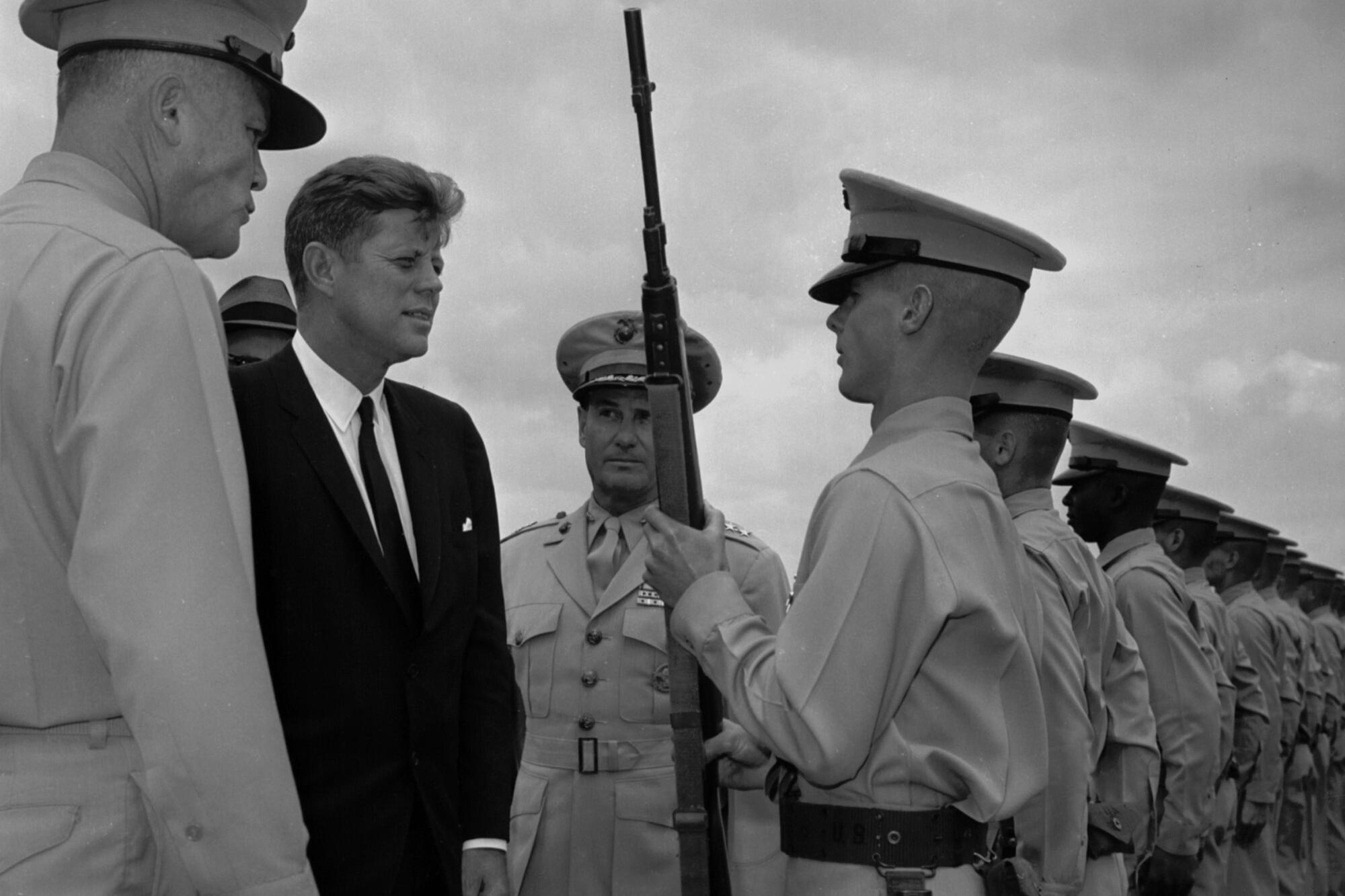 President John F. Kennedy inspects a Marine holding a rifle in a line of Marines in formation