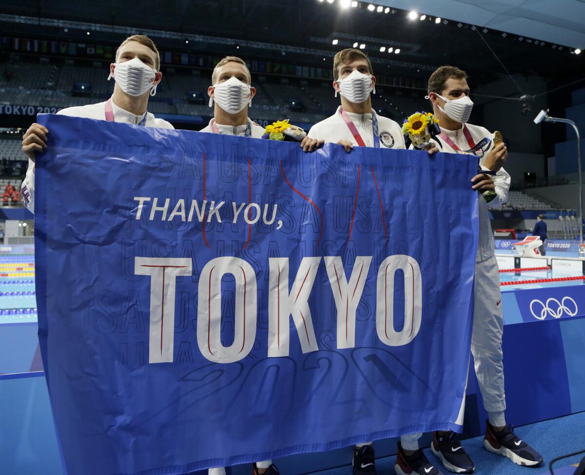 Four men in masks hold up a "Thank you, Tokyo" banner.