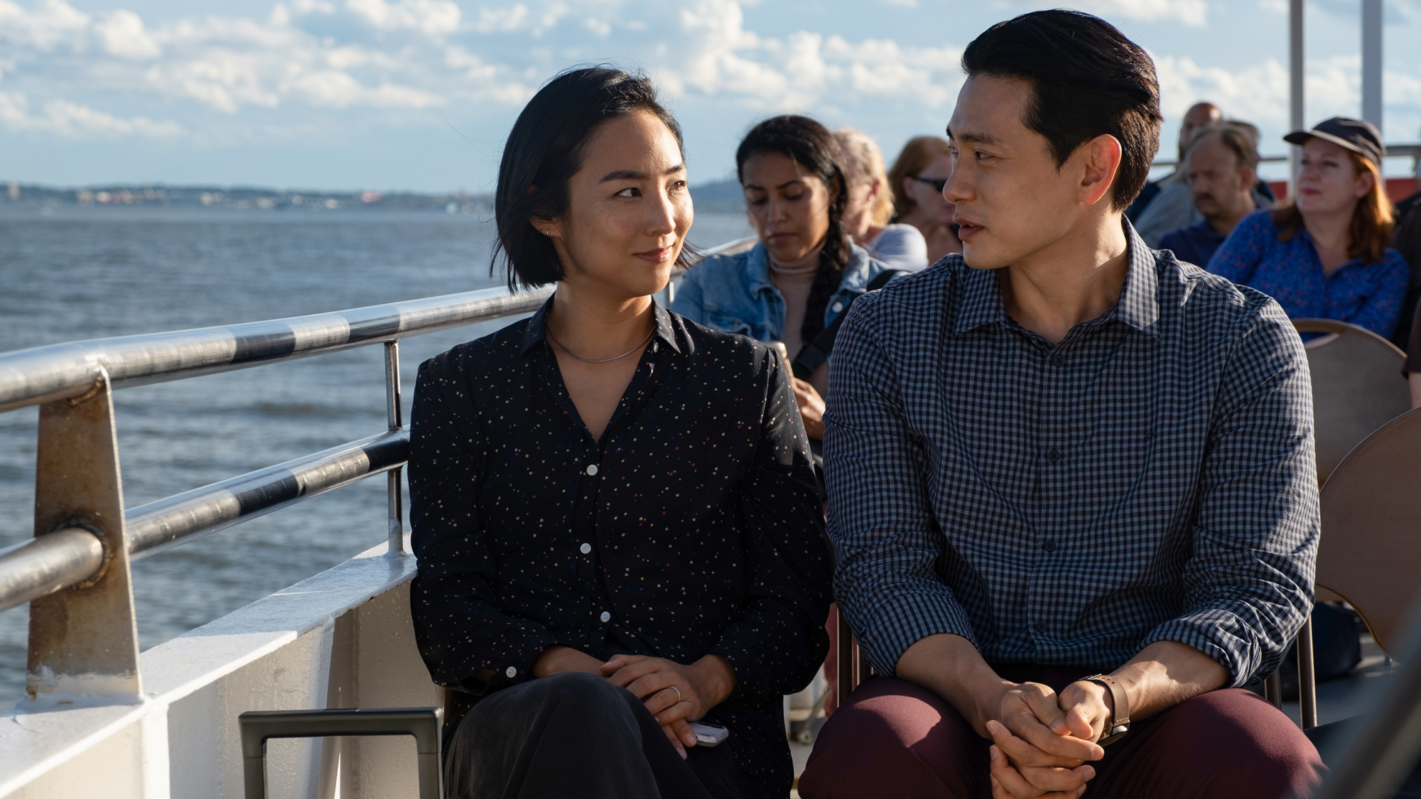 Greta Lee and Teo Yoo sit on a boat on the water with others in "Past Lives."