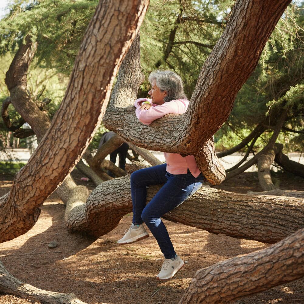 A woman sits in the entwined branches of a tree. 