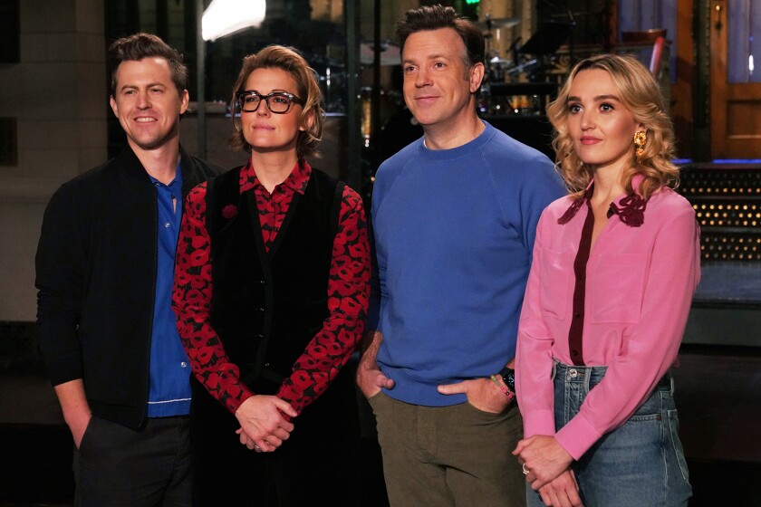 Two men and two women stand with hands in front of them on a stage.