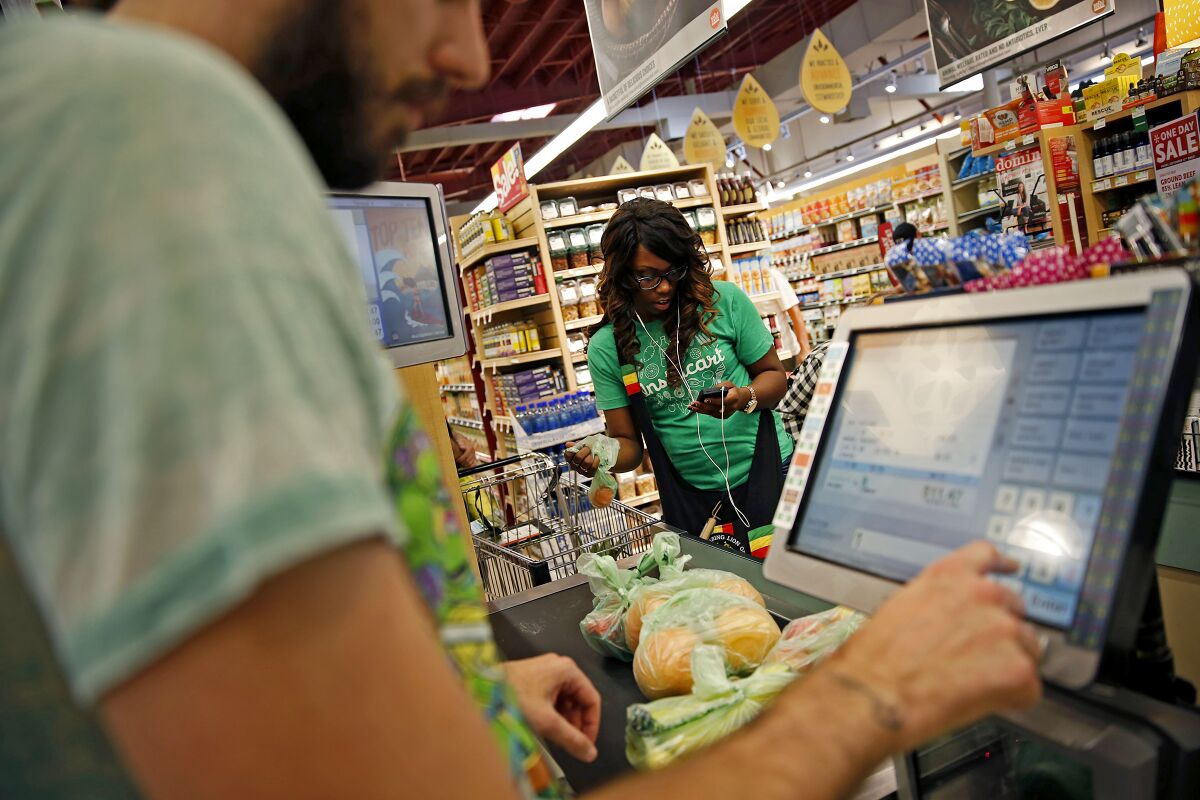 Whole Foods cashier Jason Ellsworth rings up groceries in 2014 as Instacart shopper Kara Pete uses a photo to double-check items ordered by a customer.