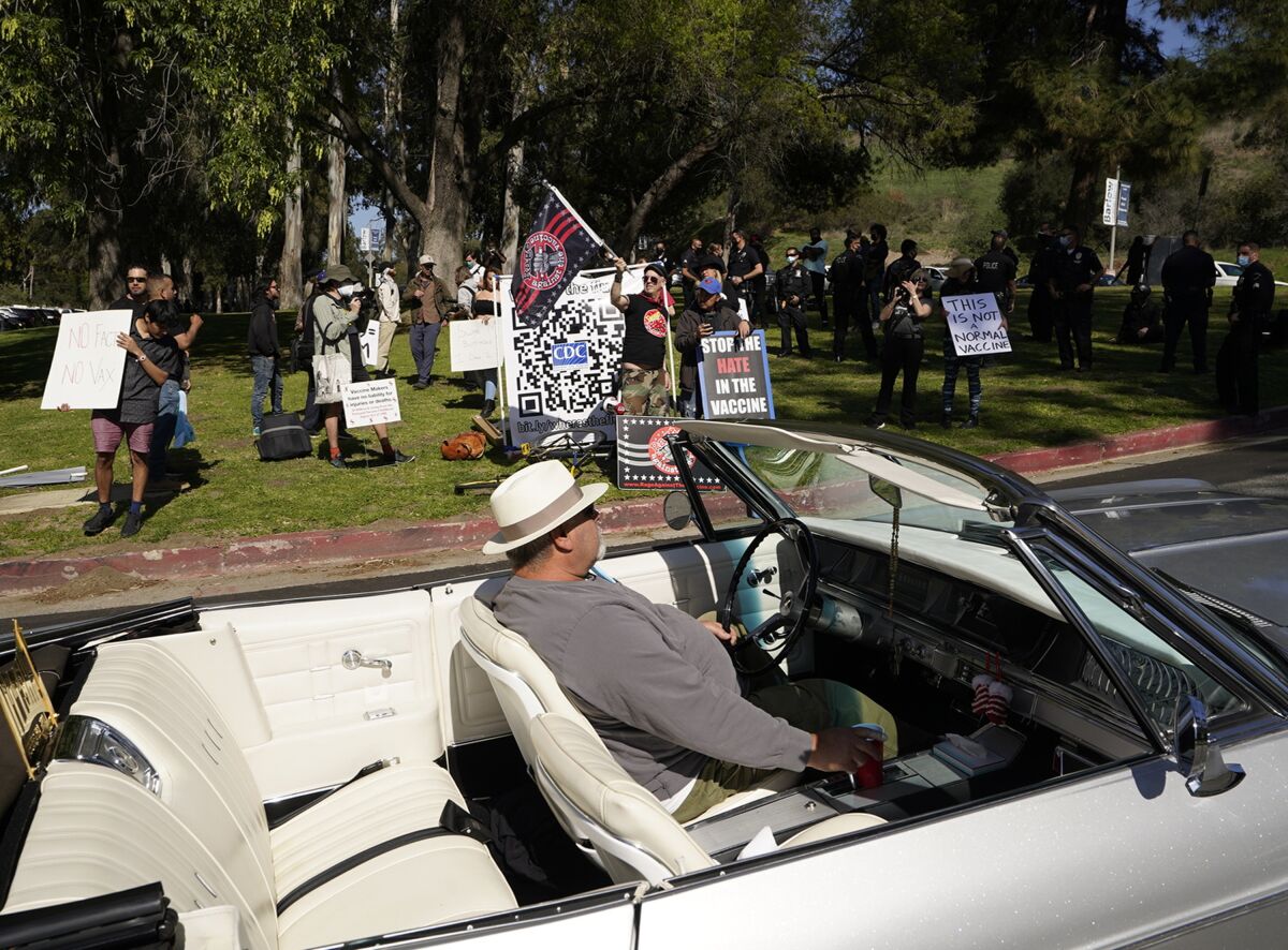 FILE - A driver in his convertible cruises past a small group of anti-COVID-19 vaccine protesters at Elysian Park, outside the Dodger Stadium vaccination mass center in Los Angeles, Saturday, Feb. 27, 2021. A federal judge has thrown out California's new 30-foot buffer zone designed to restrict protests at coronavirus vacation sites. But U.S. District Judge Dale Drozd's ruling Saturday, Oct. 30, 2021, left in place other parts of a new state law despite arguments that it infringes on free speech. (AP Photo/Damian Dovarganes, File)